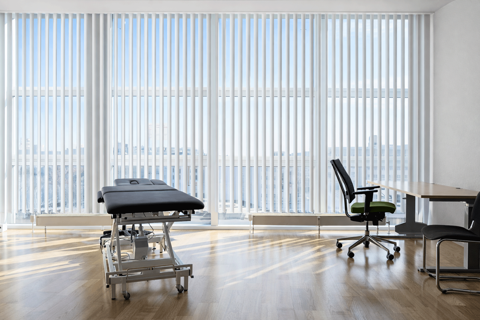 Praxisraum mit Liege und Stuhl sowie Schreibtisch